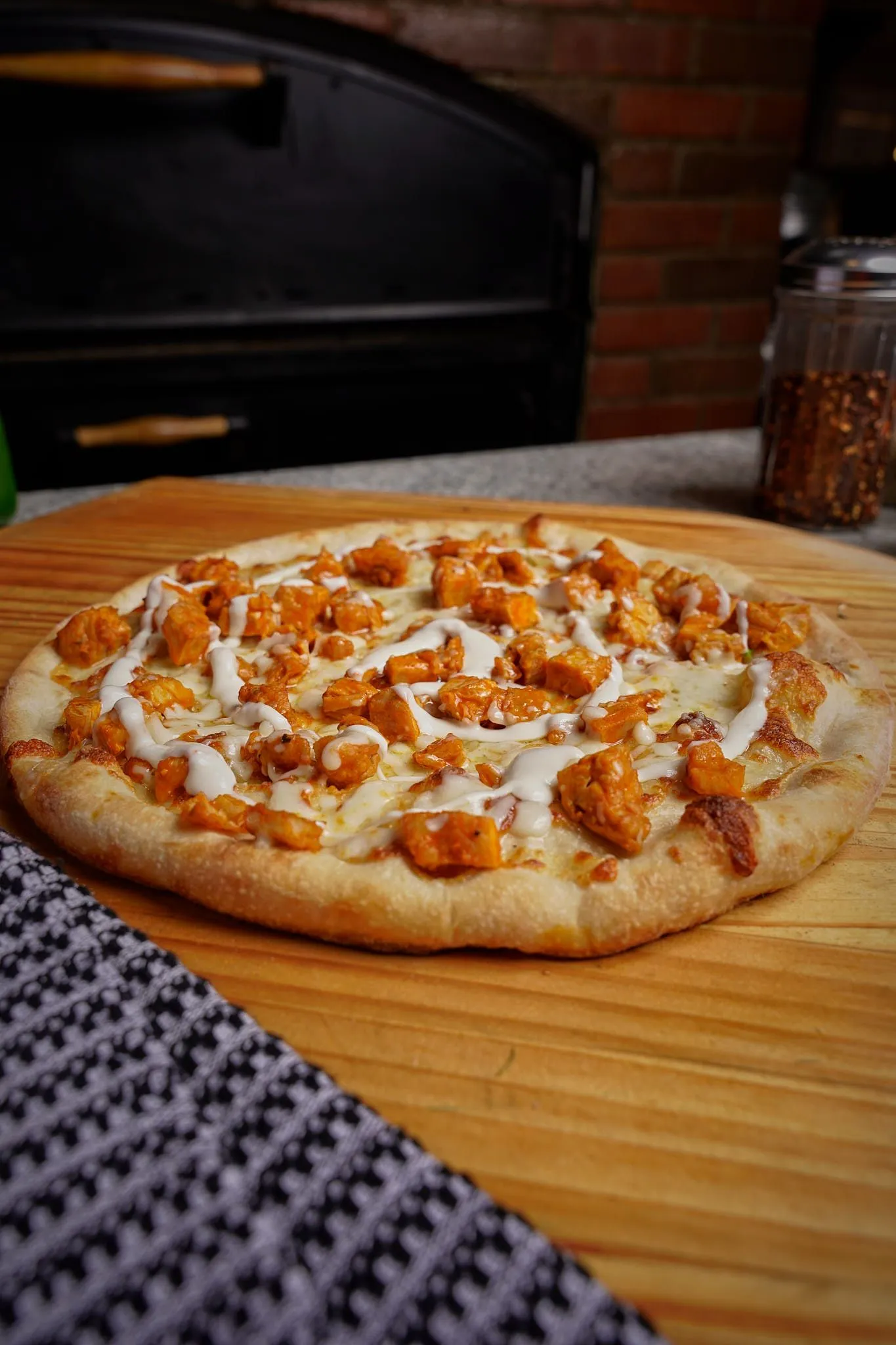 Chicken-topped pizza on a wooden board beside a brick oven at Donabella Restaurant Pizzeria