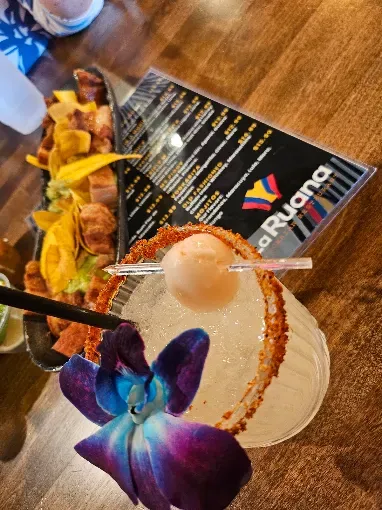 La Ruana signature cocktail garnished with an orchid, next to the Colombian food menu