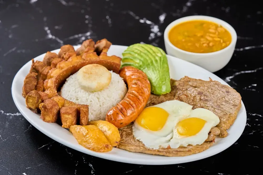 Colombian mixed plate with rice, egg, sausage, pork, avocado and beans on a white platter