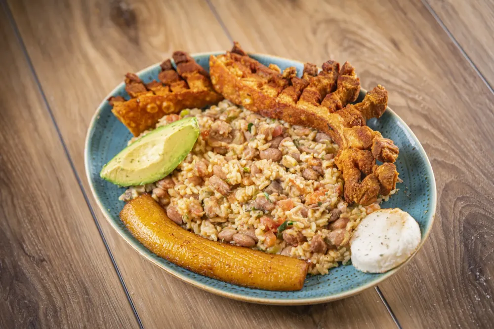 Colombian rice with beans, avocado, plantain, fried egg, and crispy pork belly on a blue plate