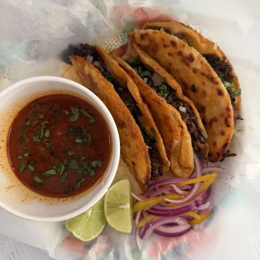 Three quesabirria tacos with a bowl of consome, lime and pickled red onion