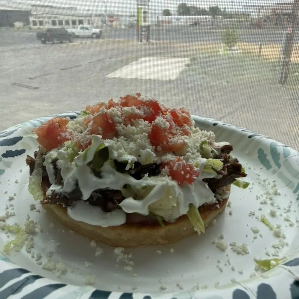 A sope topped with steak, lettuce, tomato, sour cream and queso fresco