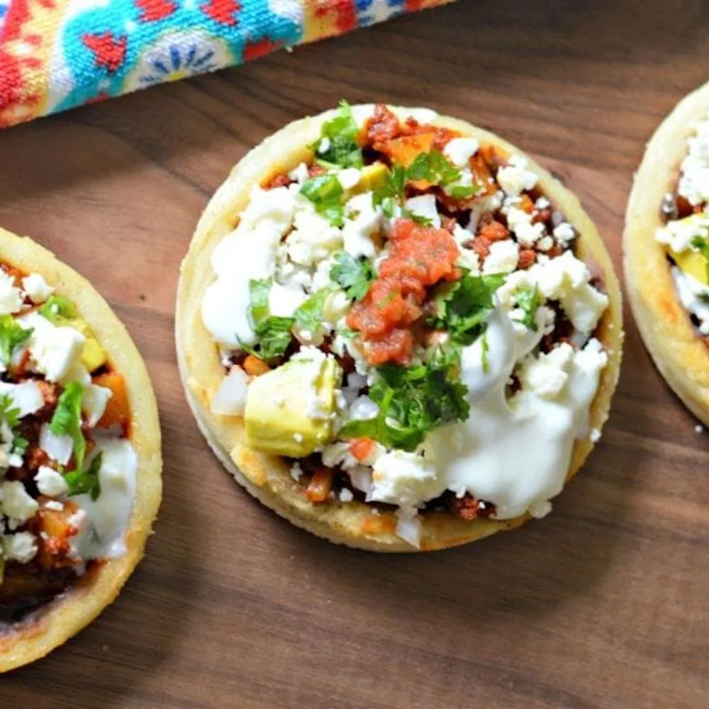 Sopes al pastor topped with queso fresco, avocado and cilantro