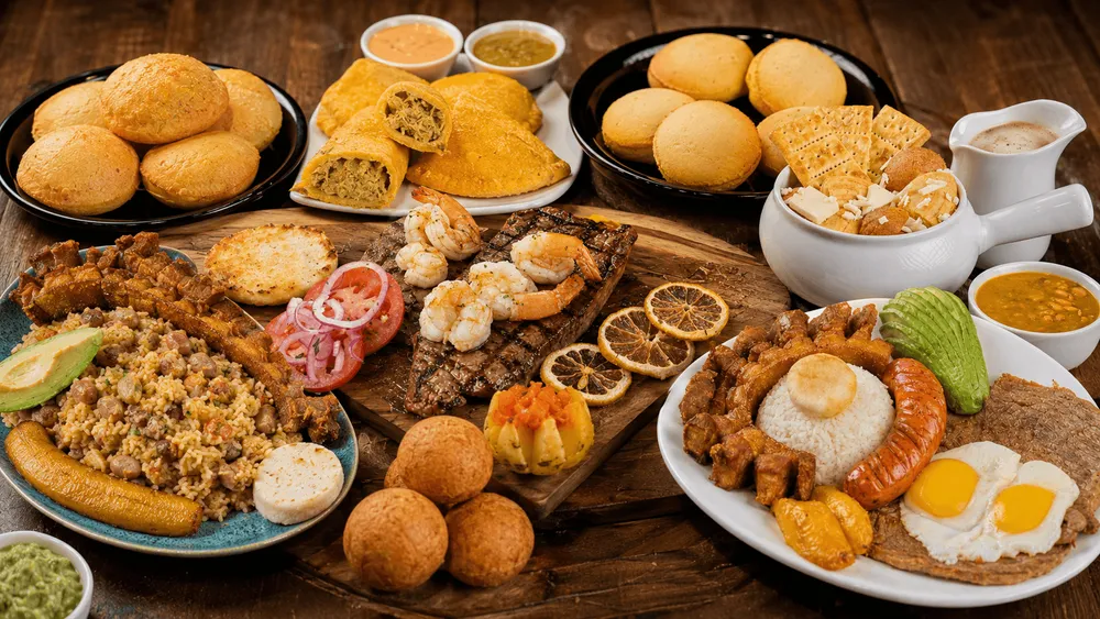 Colombian feast with arepas, empanadas, rice dishes, grilled meats, and sauces on a wooden table