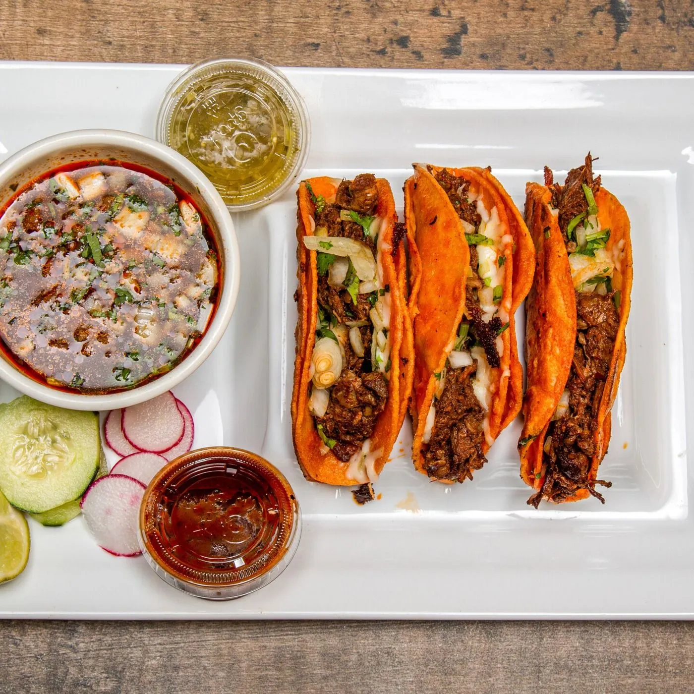 Three birria tacos with melted cheese, served with consomme and salsas